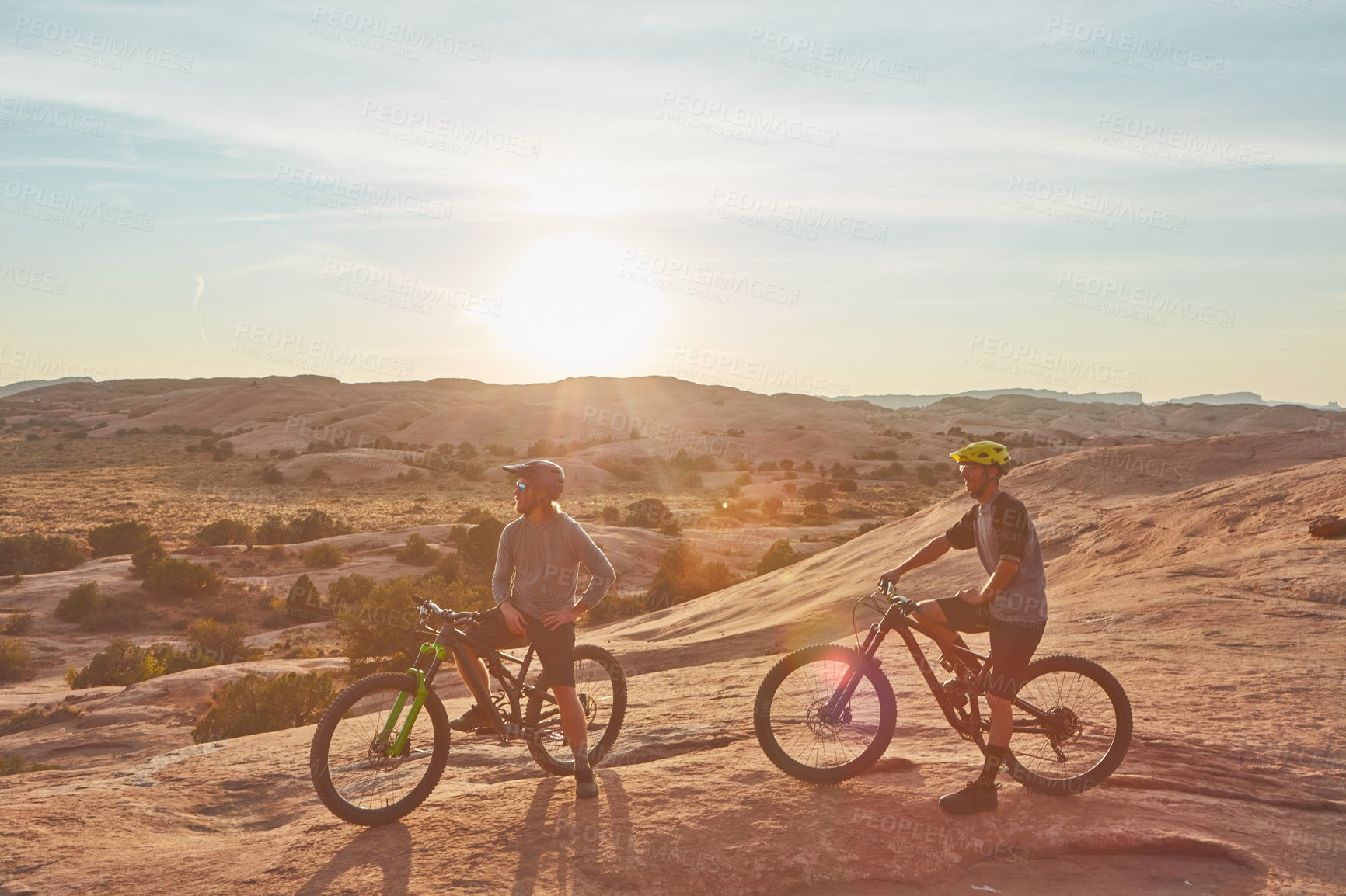 Buy stock photo Full length shot of two young male athletes mountain biking in the wilderness