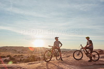 Buy stock photo Full length shot of two young male athletes mountain biking in the wilderness