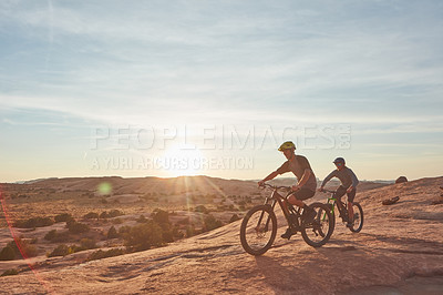 Buy stock photo Full length shot of two young male athletes mountain biking in the wilderness