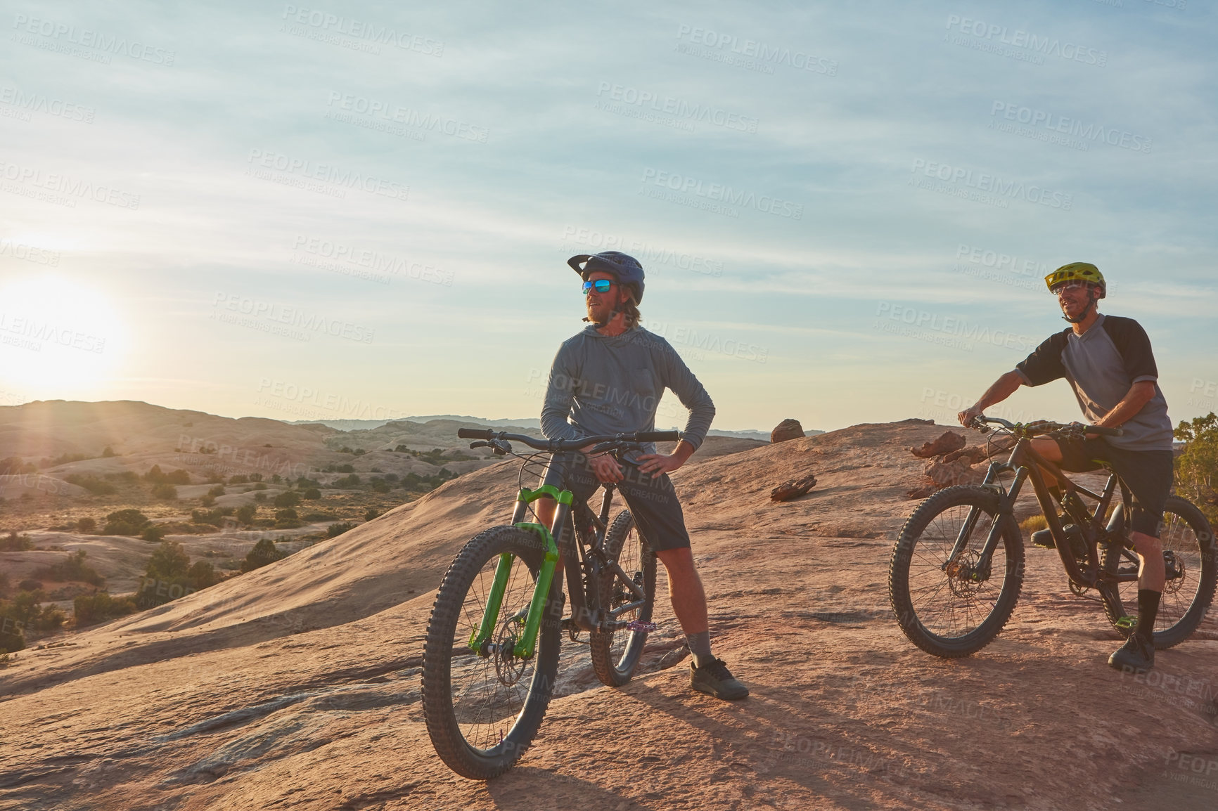 Buy stock photo Full length shot of two young male athletes mountain biking in the wilderness