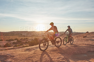 Buy stock photo Full length shot of two young male athletes mountain biking in the wilderness