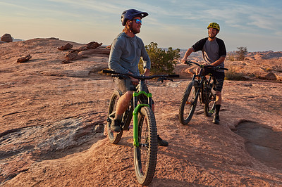 Buy stock photo Full length shot of two young male athletes mountain biking in the wilderness