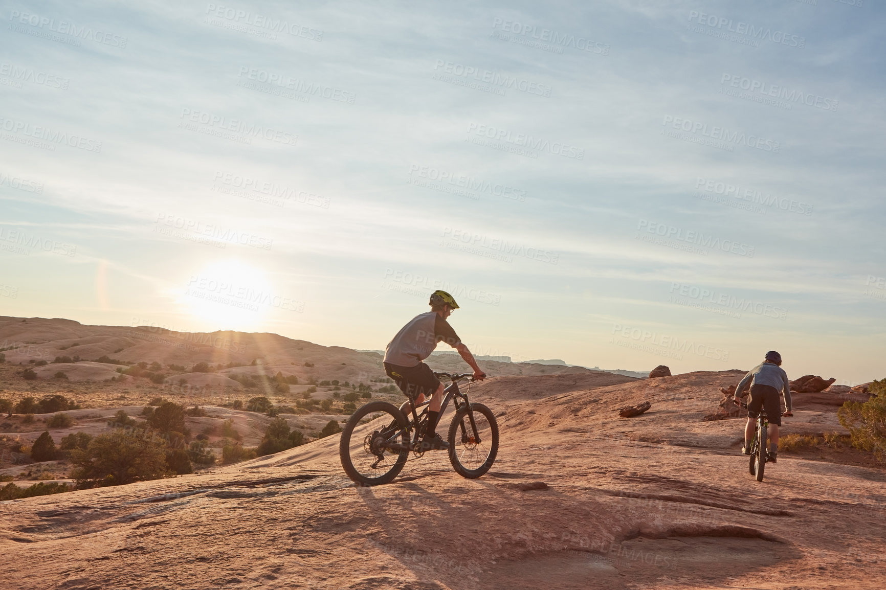 Buy stock photo Full length shot of two young male athletes mountain biking in the wilderness