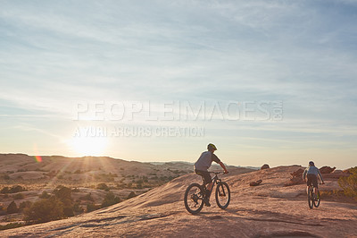 Buy stock photo Full length shot of two young male athletes mountain biking in the wilderness