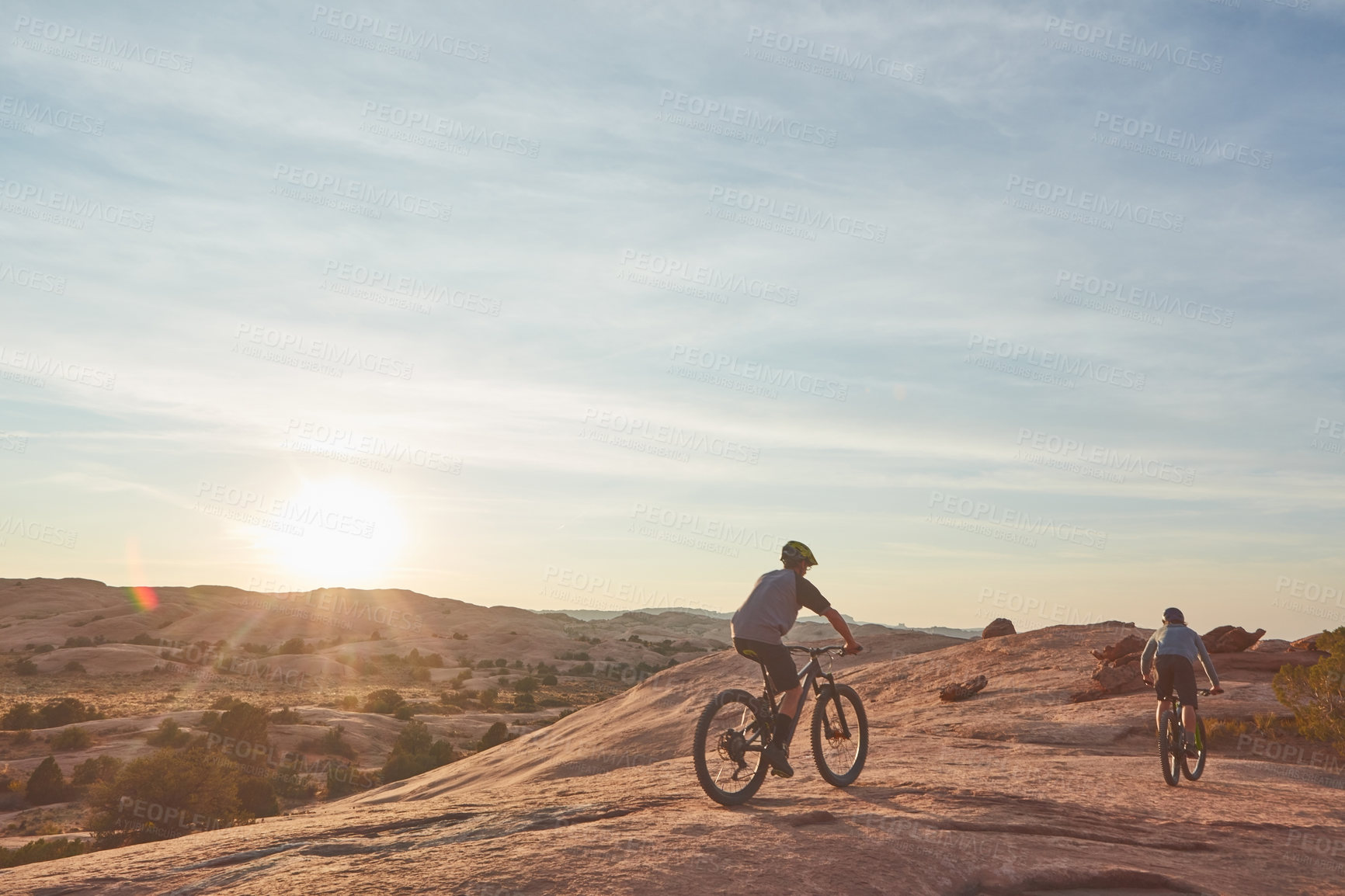 Buy stock photo Full length shot of two young male athletes mountain biking in the wilderness