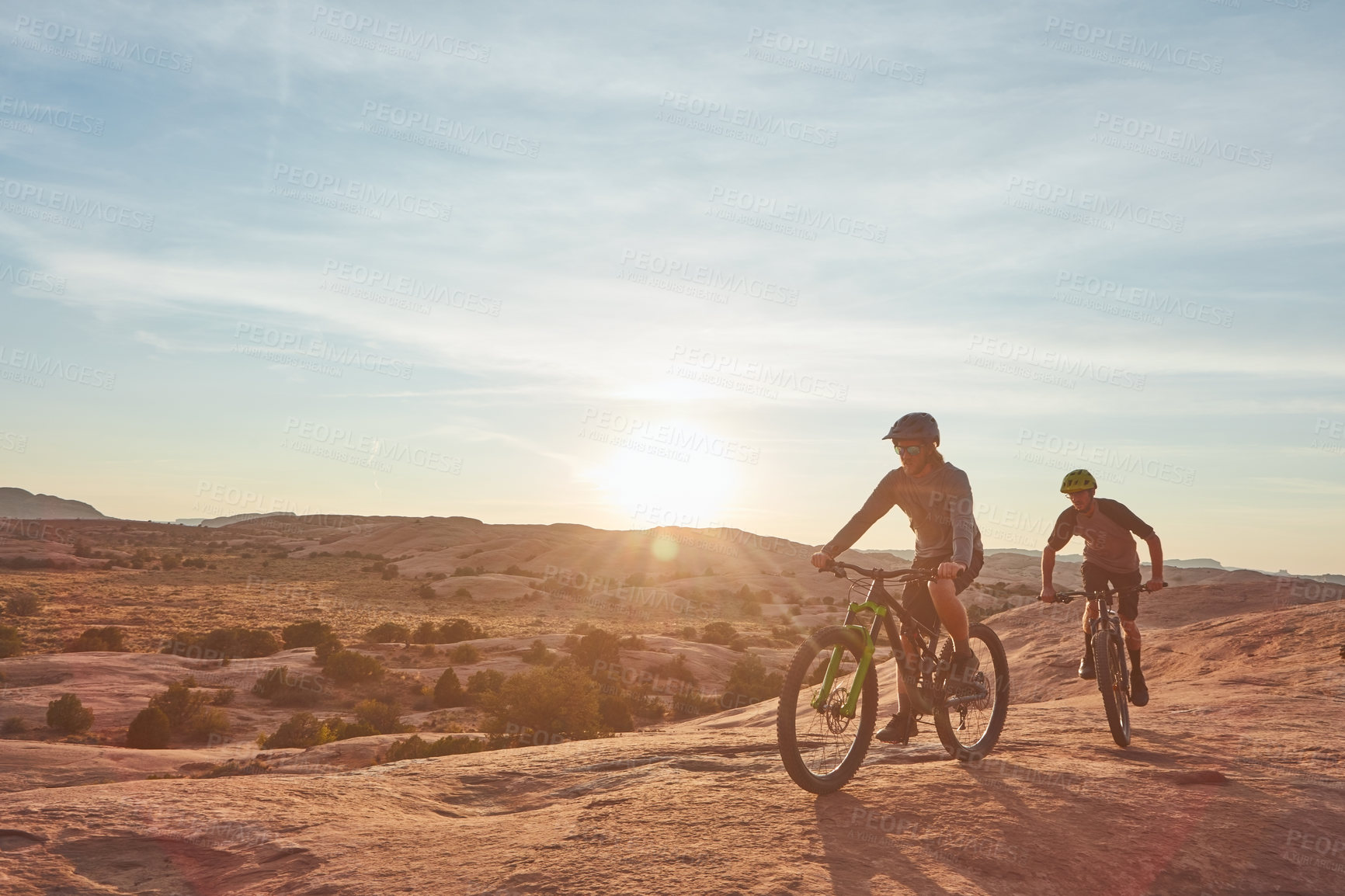 Buy stock photo Full length shot of two young male athletes mountain biking in the wilderness