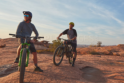 Buy stock photo Full length shot of two young male athletes mountain biking in the wilderness