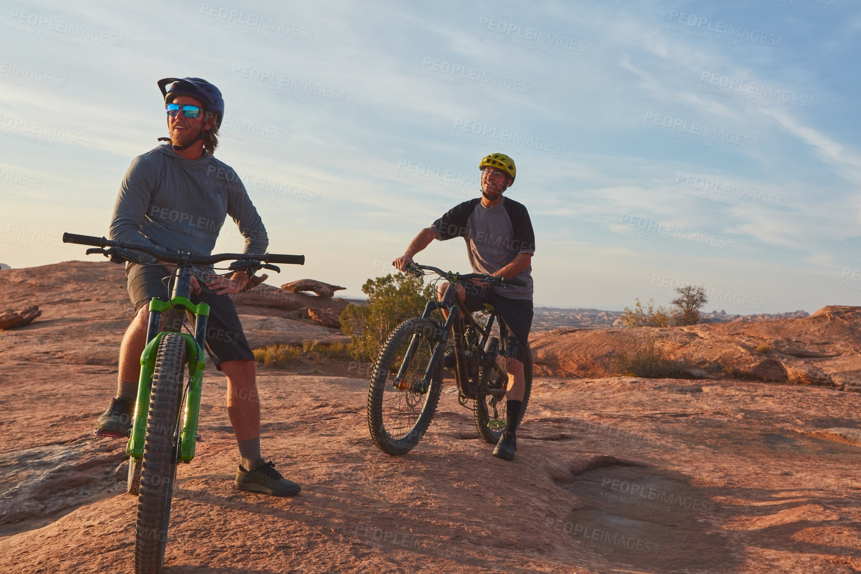 Buy stock photo Full length shot of two young male athletes mountain biking in the wilderness