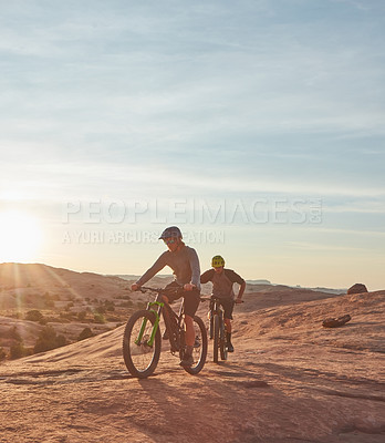 Buy stock photo Full length shot of two young male athletes mountain biking in the wilderness