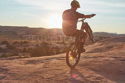 Buy stock photo Full length shot of a young male athlete popping a wheelie while mountain biking in the wilderness