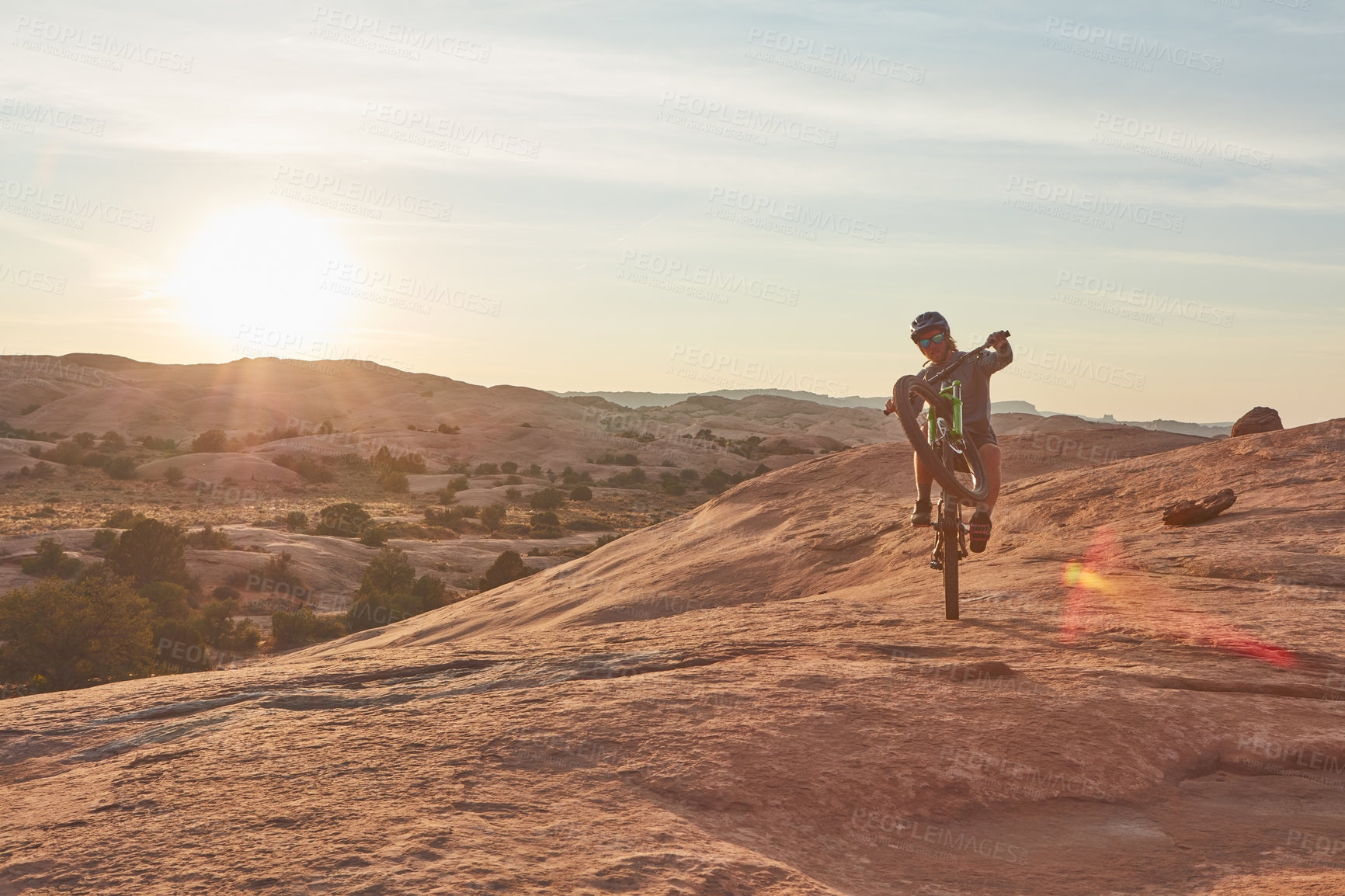 Buy stock photo Full length shot of a young male athlete popping a wheelie while mountain biking in the wilderness