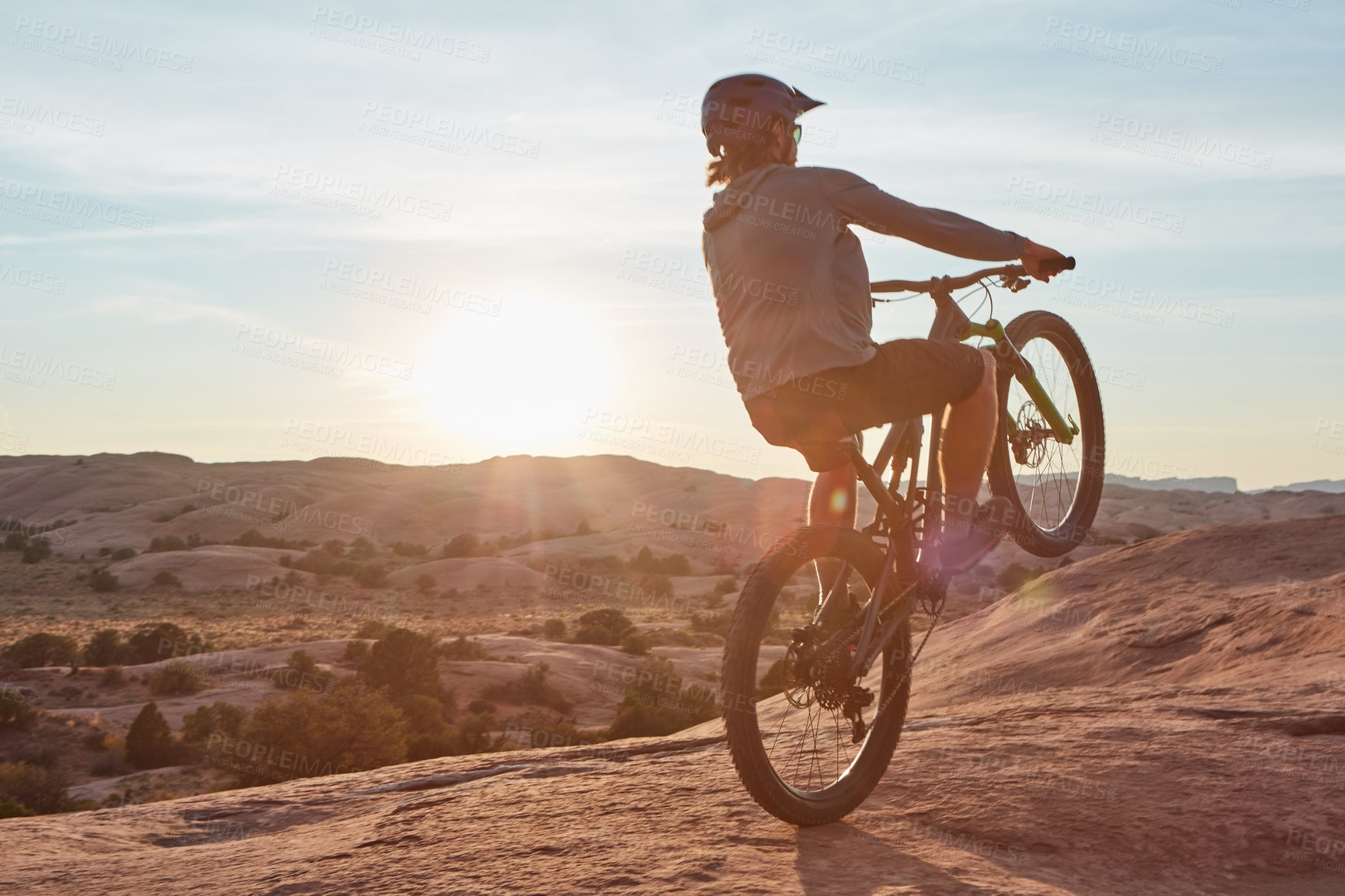 Buy stock photo Full length shot of a young male athlete popping a wheelie while mountain biking in the wilderness