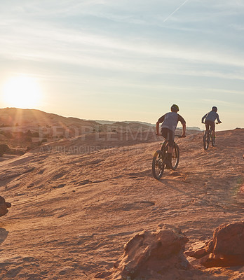 Buy stock photo Full length shot of two young male athletes mountain biking in the wilderness