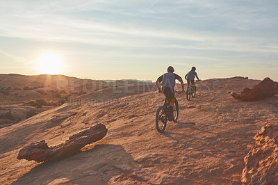 Buy stock photo Full length shot of two young male athletes mountain biking in the wilderness