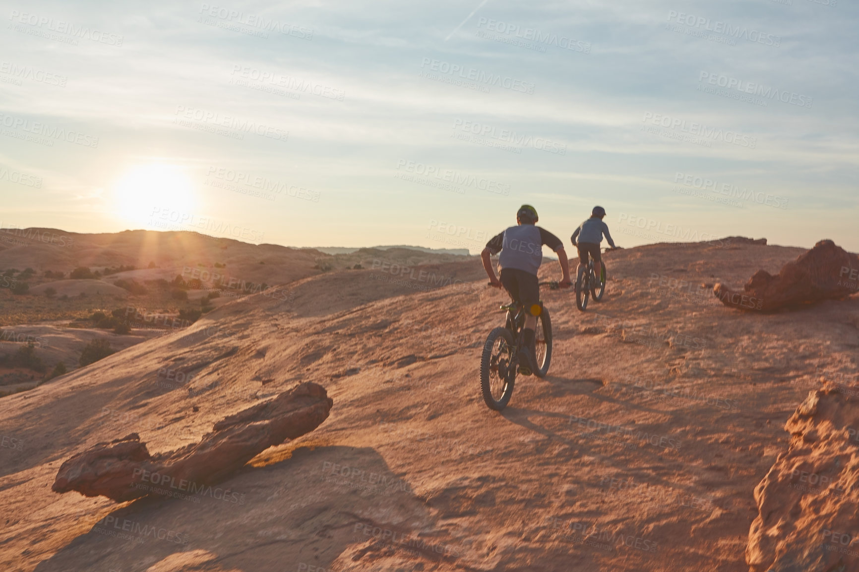 Buy stock photo Full length shot of two young male athletes mountain biking in the wilderness