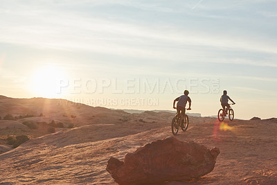 Buy stock photo Full length shot of two young male athletes mountain biking in the wilderness