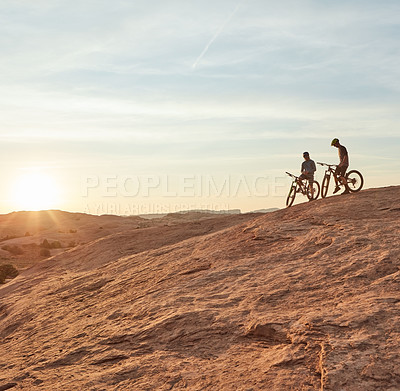 Buy stock photo Full length shot of two young male athletes mountain biking in the wilderness