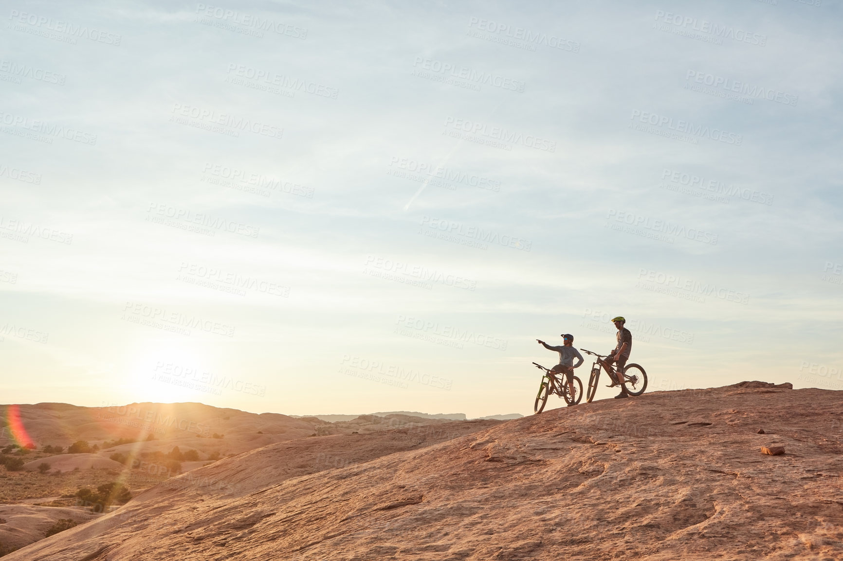 Buy stock photo Full length shot of two young male athletes mountain biking in the wilderness