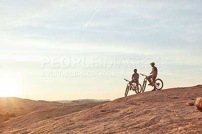 Buy stock photo Full length shot of two young male athletes mountain biking in the wilderness