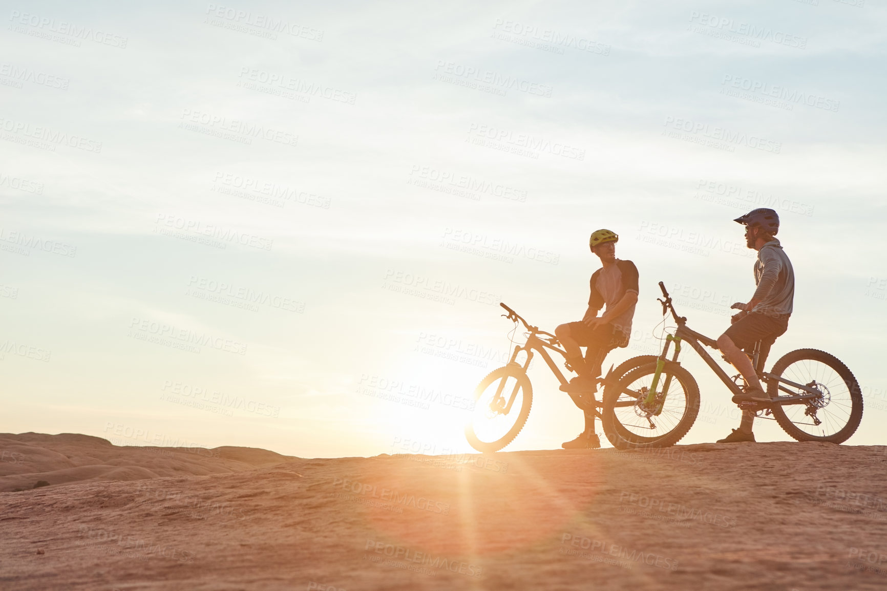 Buy stock photo Full length shot of two young male athletes mountain biking in the wilderness