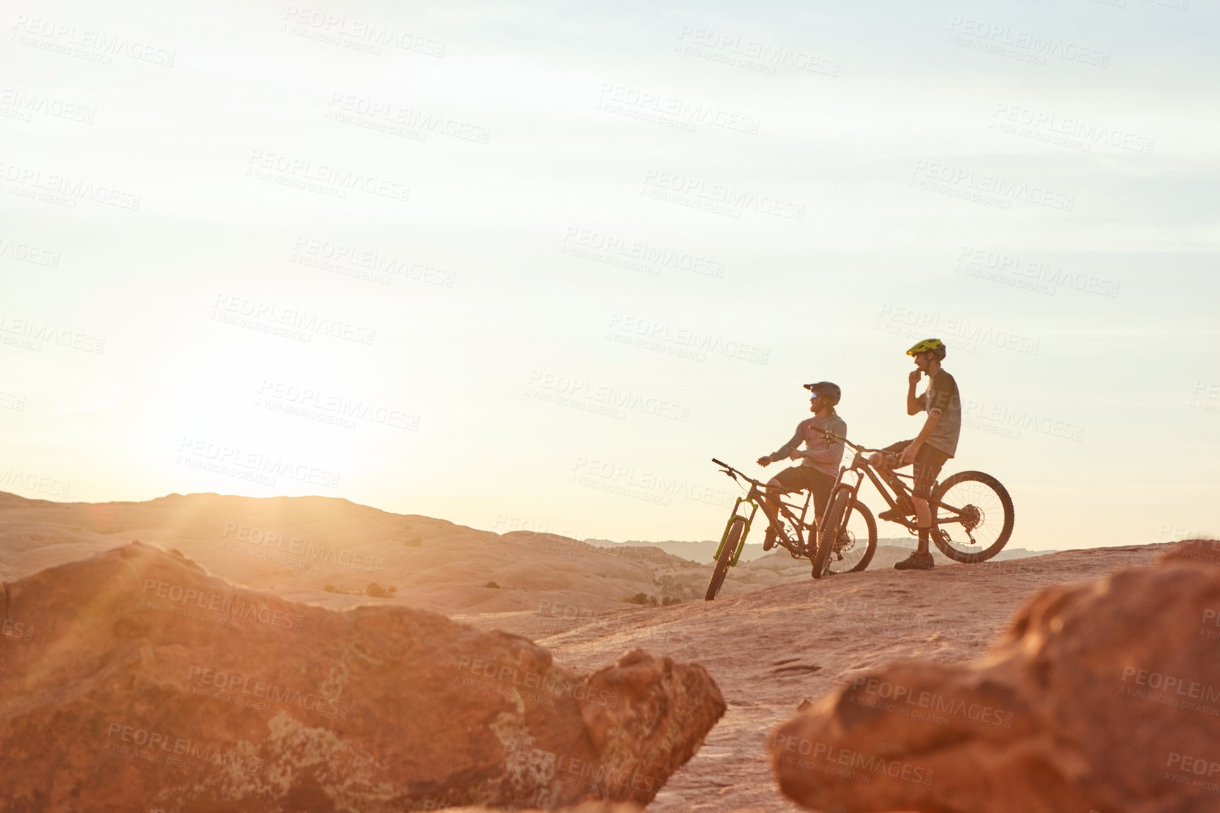 Buy stock photo Full length shot of two young male athletes mountain biking in the wilderness