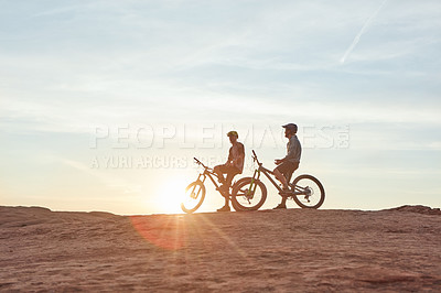 Buy stock photo Full length shot of two young male athletes mountain biking in the wilderness