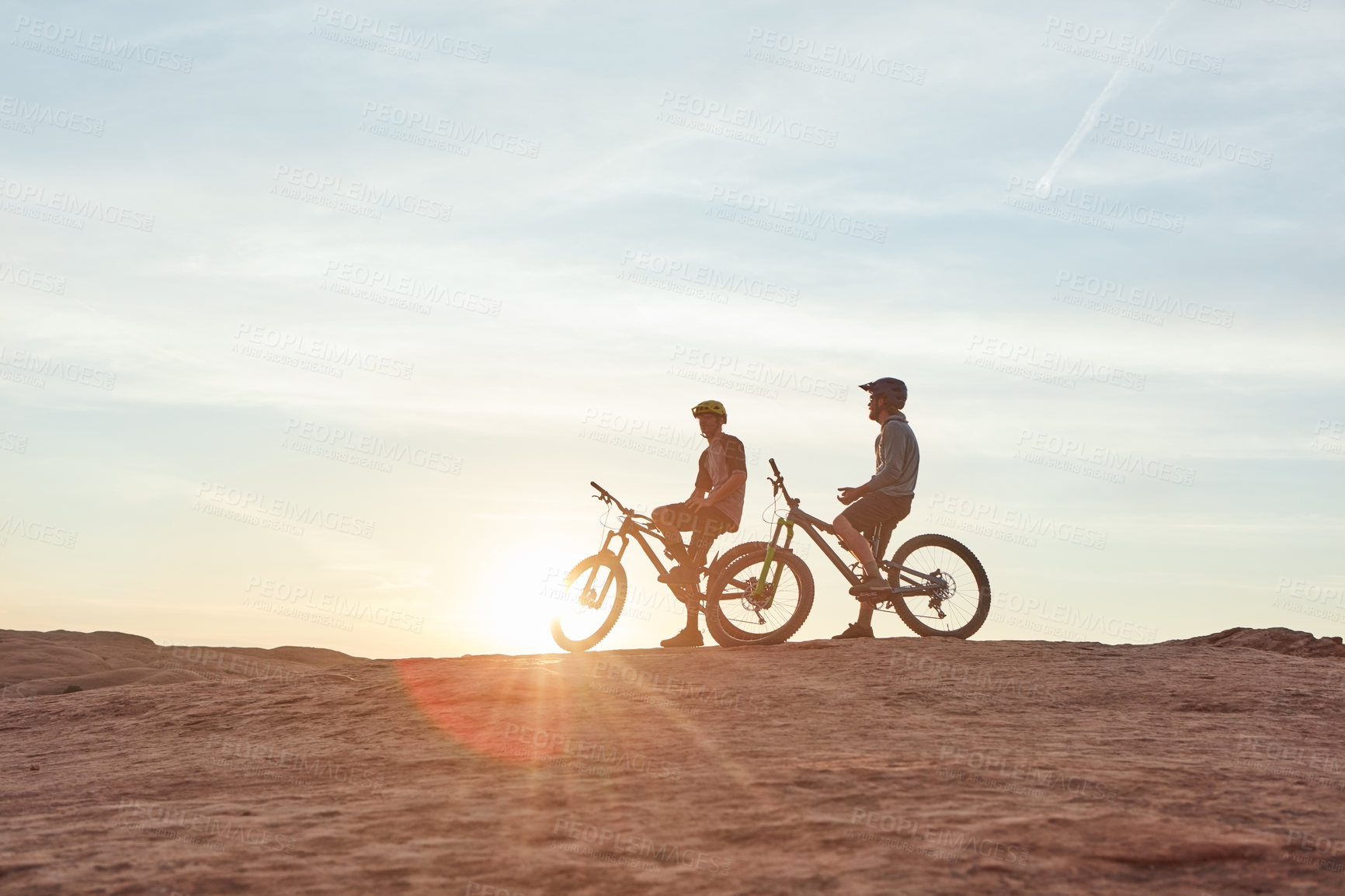 Buy stock photo Full length shot of two young male athletes mountain biking in the wilderness