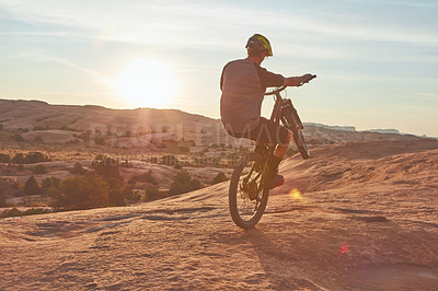 Buy stock photo Full length shot of a young male athlete popping a wheelie while mountain biking in the wilderness