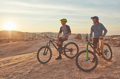 Buy stock photo Full length shot of two young male athletes mountain biking in the wilderness