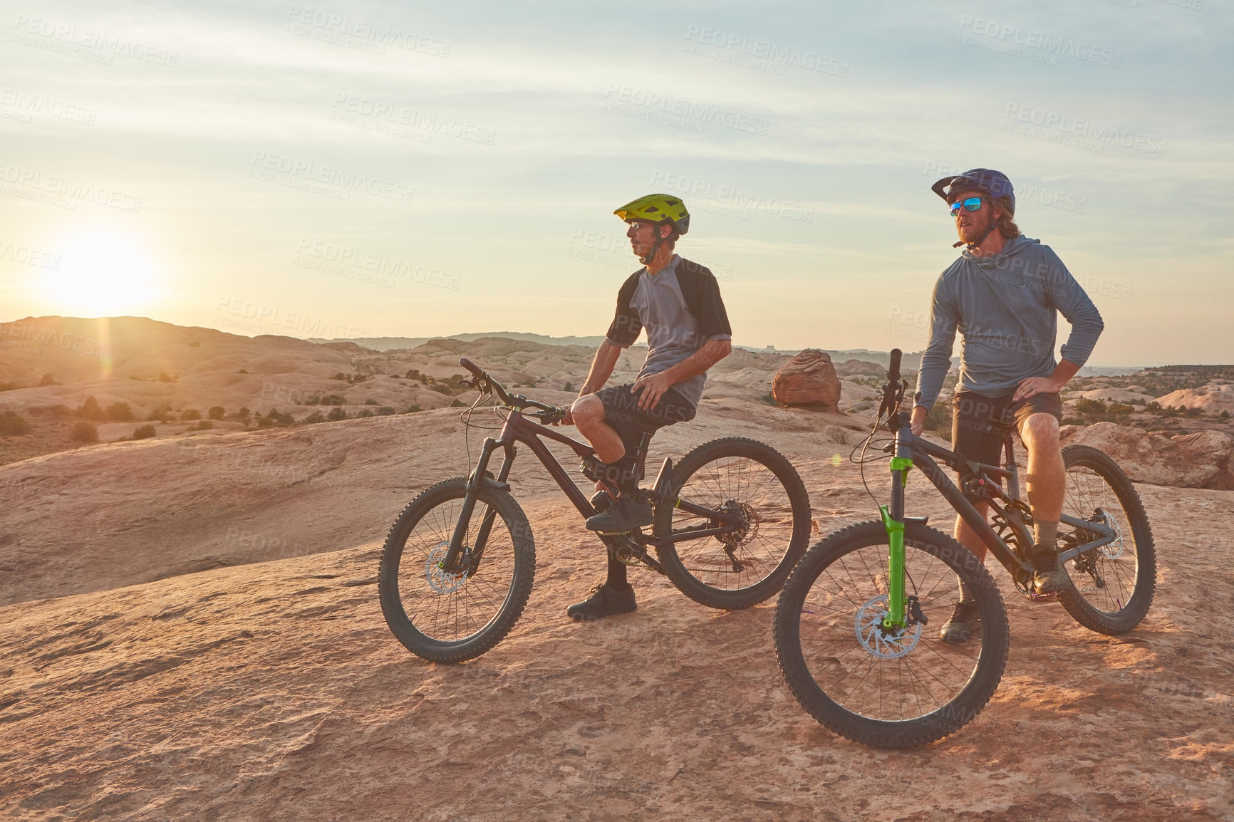 Buy stock photo Full length shot of two young male athletes mountain biking in the wilderness