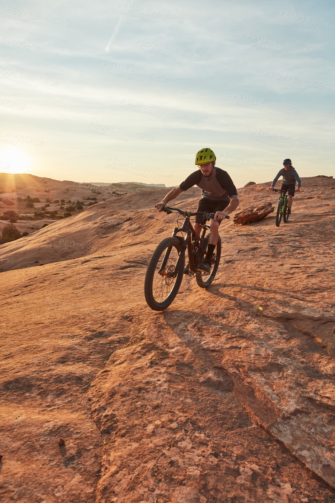 Buy stock photo Full length shot of two young male athletes mountain biking in the wilderness