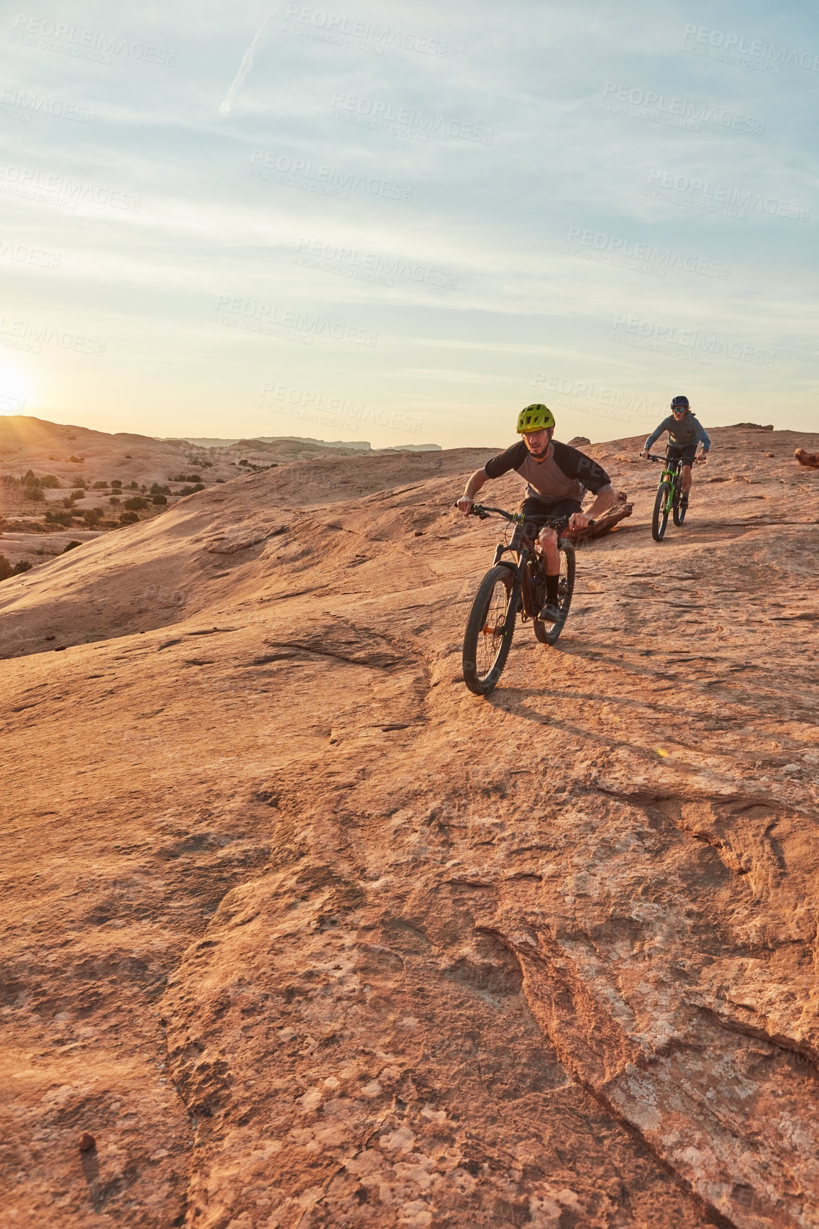 Buy stock photo Full length shot of two young male athletes mountain biking in the wilderness