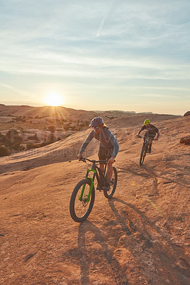 Buy stock photo Full length shot of two young male athletes mountain biking in the wilderness