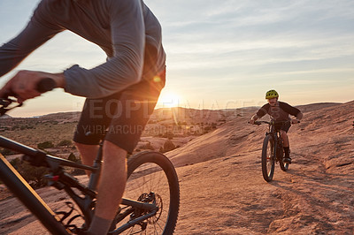 Buy stock photo Full length shot of two young male athletes mountain biking in the wilderness