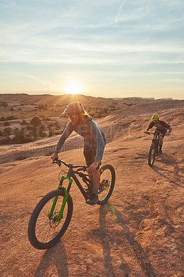 Buy stock photo Full length shot of two young male athletes mountain biking in the wilderness