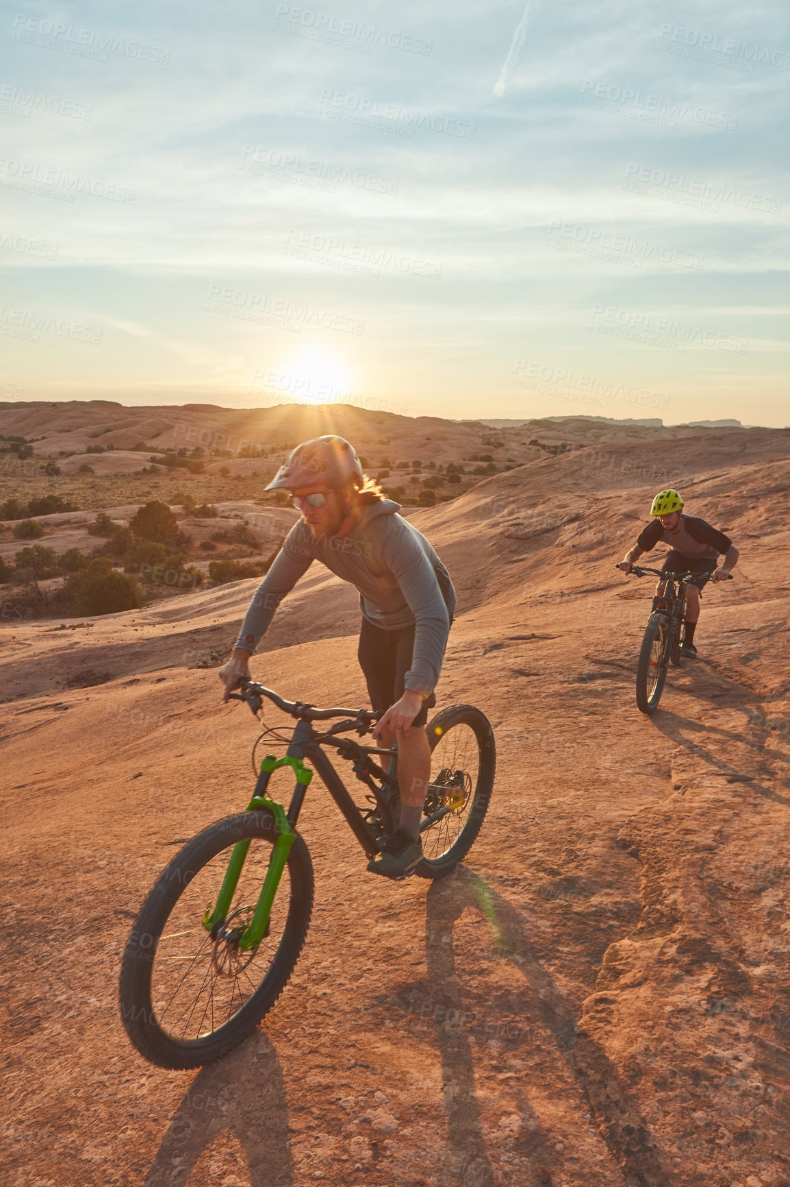 Buy stock photo Full length shot of two young male athletes mountain biking in the wilderness