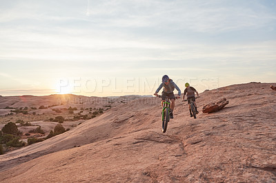 Buy stock photo Full length shot of two young male athletes mountain biking in the wilderness