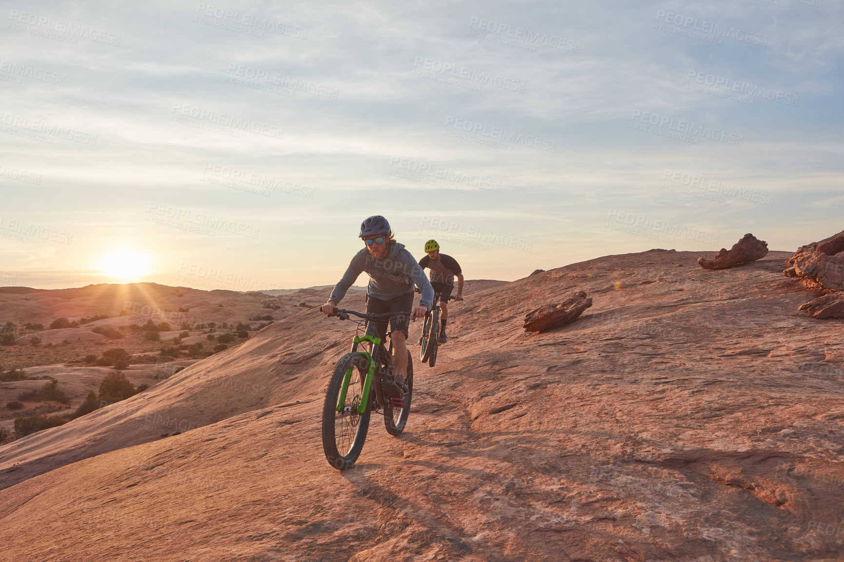 Buy stock photo Full length shot of two young male athletes mountain biking in the wilderness