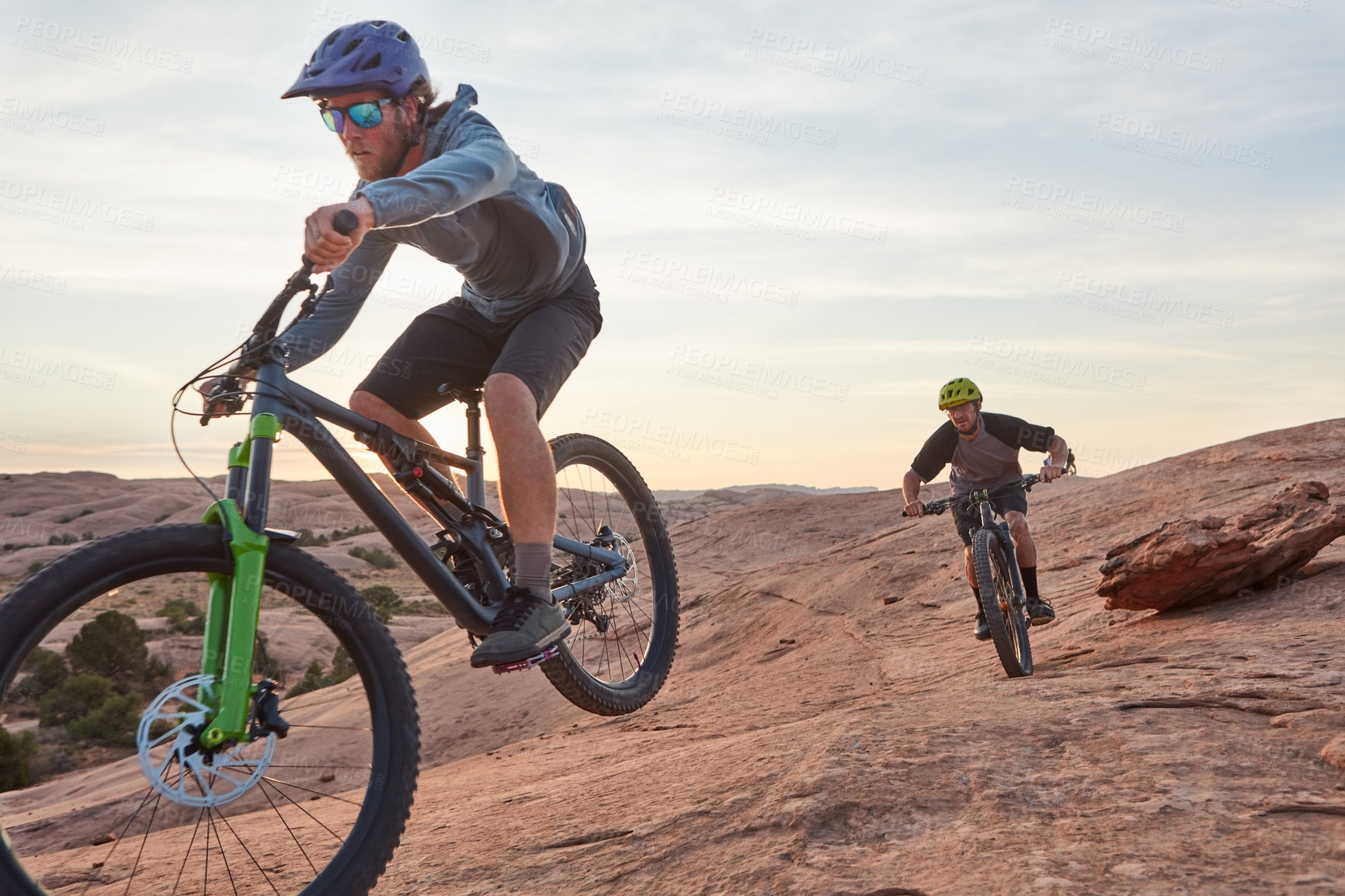 Buy stock photo Full length shot of two young male athletes mountain biking in the wilderness