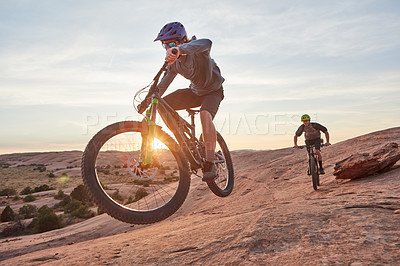 Buy stock photo Full length shot of two young male athletes mountain biking in the wilderness