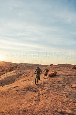 Buy stock photo Full length shot of two young male athletes mountain biking in the wilderness