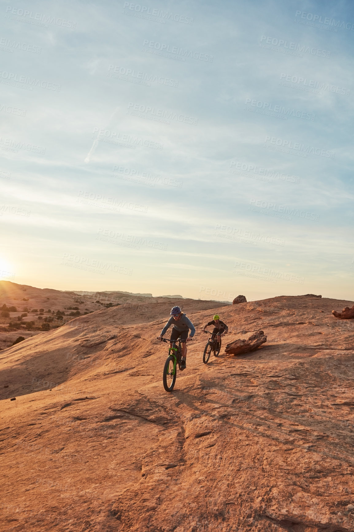 Buy stock photo Full length shot of two young male athletes mountain biking in the wilderness