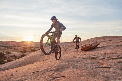 Buy stock photo Full length shot of two young male athletes mountain biking in the wilderness