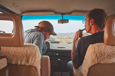 Buy stock photo Shot of two men smoking together while out on a road trip