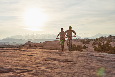 Buy stock photo Full length shot of two athletic men mountain biking through the wilderness