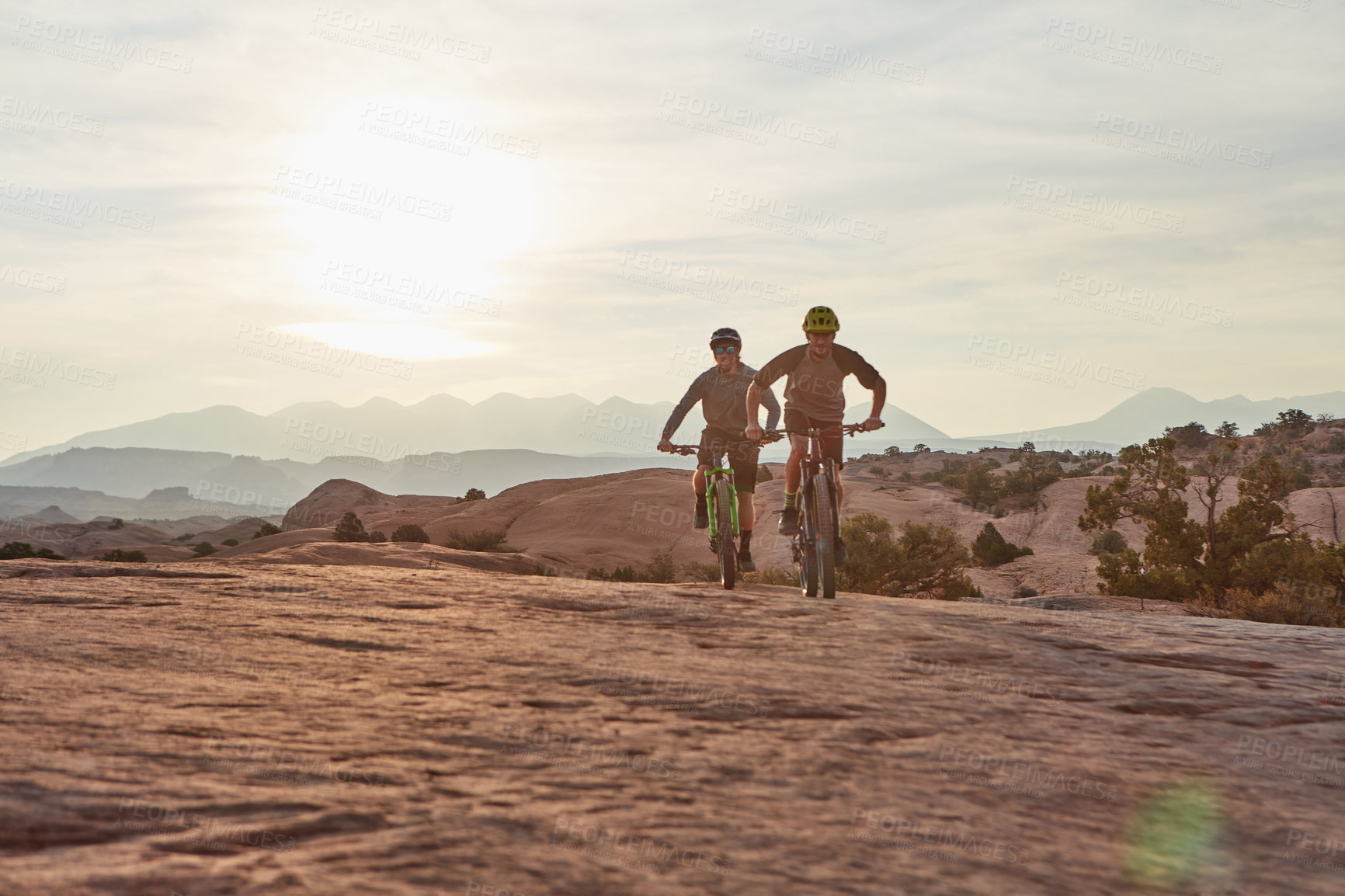 Buy stock photo Full length shot of two athletic men mountain biking through the wilderness