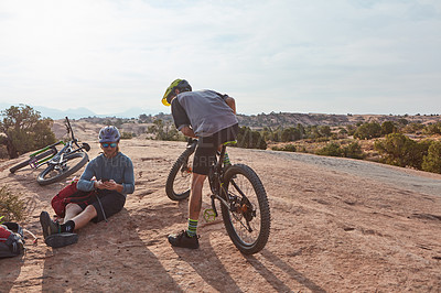 Buy stock photo Full length shot of two athletic men taking a break while mountain biking through the wilderness