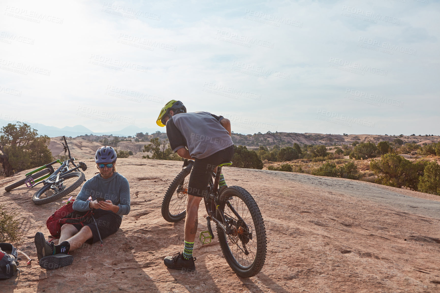 Buy stock photo Full length shot of two athletic men taking a break while mountain biking through the wilderness