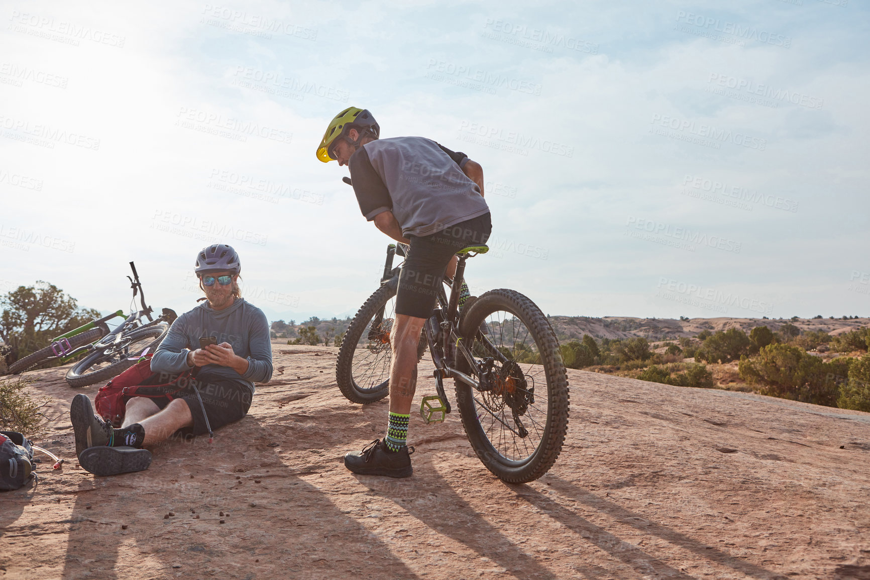 Buy stock photo Full length shot of two athletic men taking a break while mountain biking through the wilderness