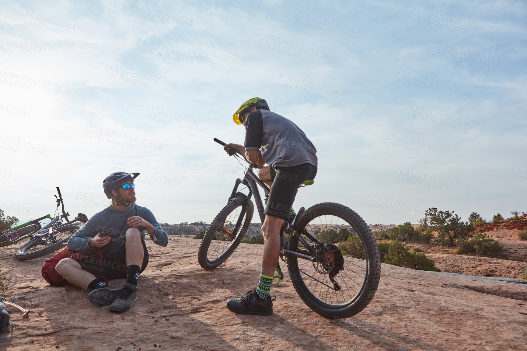 Buy stock photo Full length shot of two athletic men taking a break while mountain biking through the wilderness